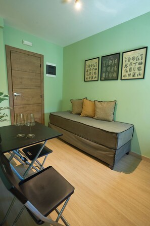 A room with a wooden door, a sofa with cushions, a table with two glasses, and framed botanical illustrations on the wall. - Harmony 89 (Palaio Faliro)