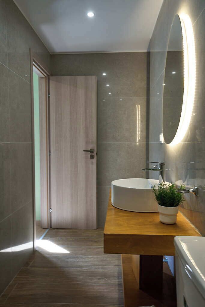 A modern bathroom with a wooden vanity, a white sink, and a large mirror.