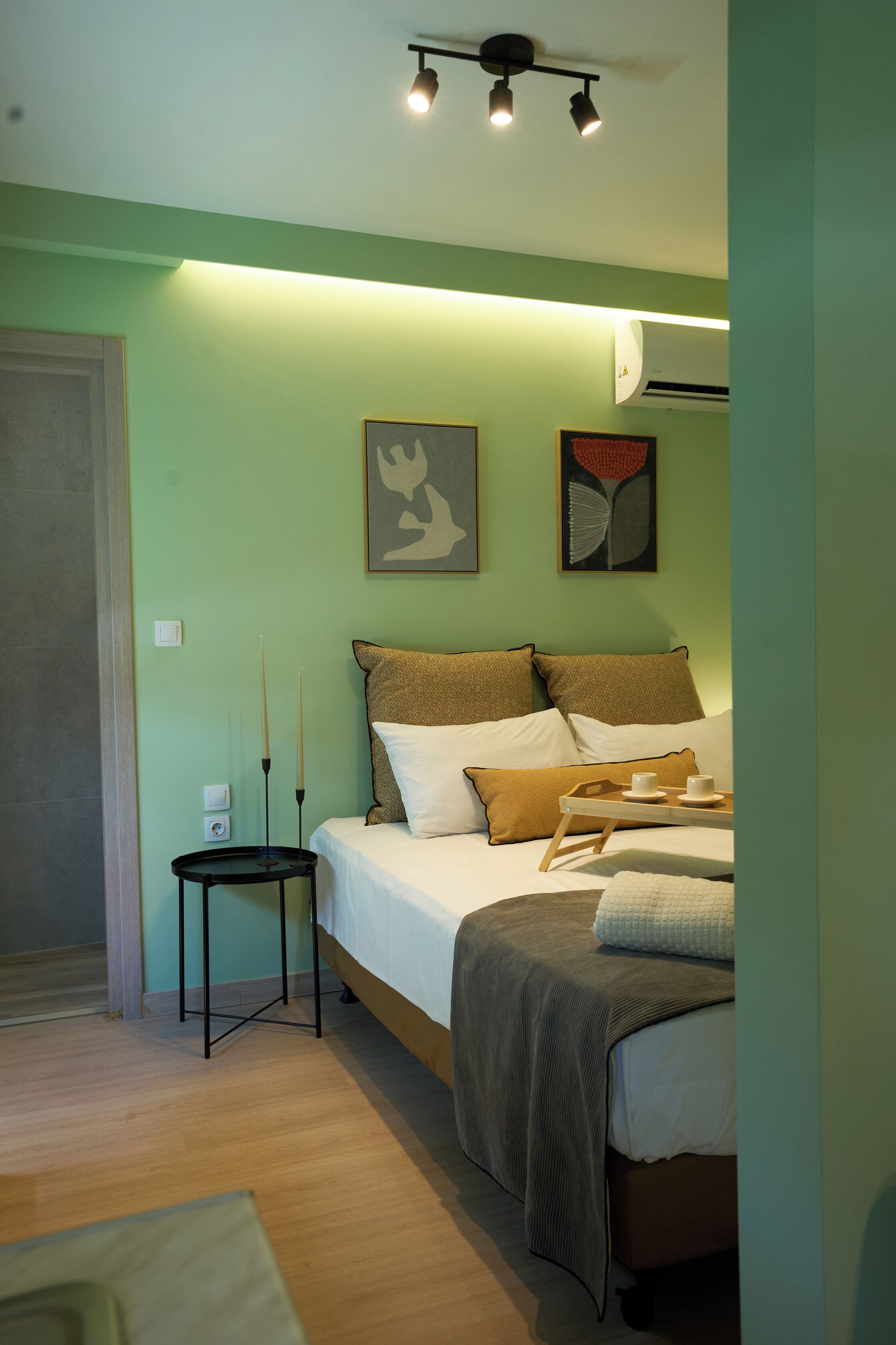 Un dormitorio con cama, mesita de noche, dos cuadros colgados en la pared y una lámpara en el techo.