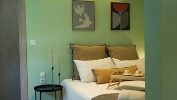 Un dormitorio con cama, mesita de noche, dos cuadros colgados en la pared y una lámpara en el techo.