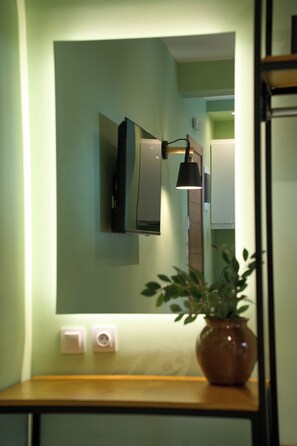 A bathroom with a mirror, a wall-mounted light fixture, and a potted plant on a wooden counter.