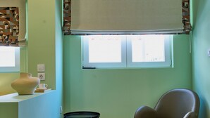 Une pièce avec une fenêtre, une chaise, une petite table et un climatiseur fixé au mur.
