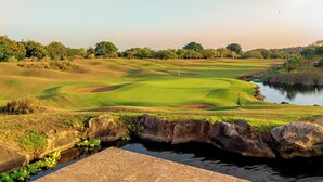 Egy golfpálya, melynek része egy tó, fák és a tiszta égbolt.