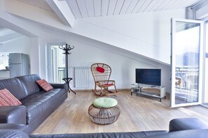 Ein modernes Wohnzimmer mit einer Couch, einem Fernseher, einem Korbsessel und einem großen Fenster.