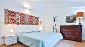 Una camera da letto con un letto, un comodino, una cassettiera, un arazzo e un appendiabiti.