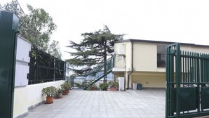 Un cortile recintato con piante in vaso, una scalinata e un edificio dalla facciata beige.
