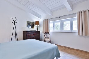 Ein Schlafzimmer mit Bett, Schminktisch, Stuhl, Lampe und einem Fenster mit Vorhängen.