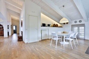 Eine geräumige Küche mit weißen Schränken, ein Essbereich mit rundem Tisch und Stühlen sowie eine hohe Decke mit sichtbaren Balken.