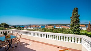 Une terrasse avec une table et des chaises, d’où l’on peut admirer une ville côtière avec ses bâtiments et un ciel bleu dégagé.
