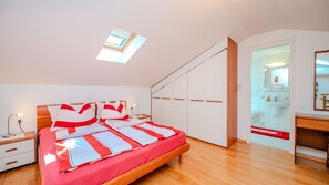 Une chambre à coucher comprenant un lit, des tables de chevet, une armoire, un miroir et une salle de bain visible à travers une porte ouverte.