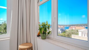 Una habitación con un ventanal grande, un taburete de mimbre y una planta en maceta.