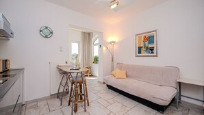 Una sala de estar moderna con un sofá beige, una mesa de comedor con sillas, una zona de cocina y un cuadro en la pared.