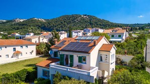 Zona residencial con casas de techos rojos y paneles solares, rodeada de vegetación y colinas.