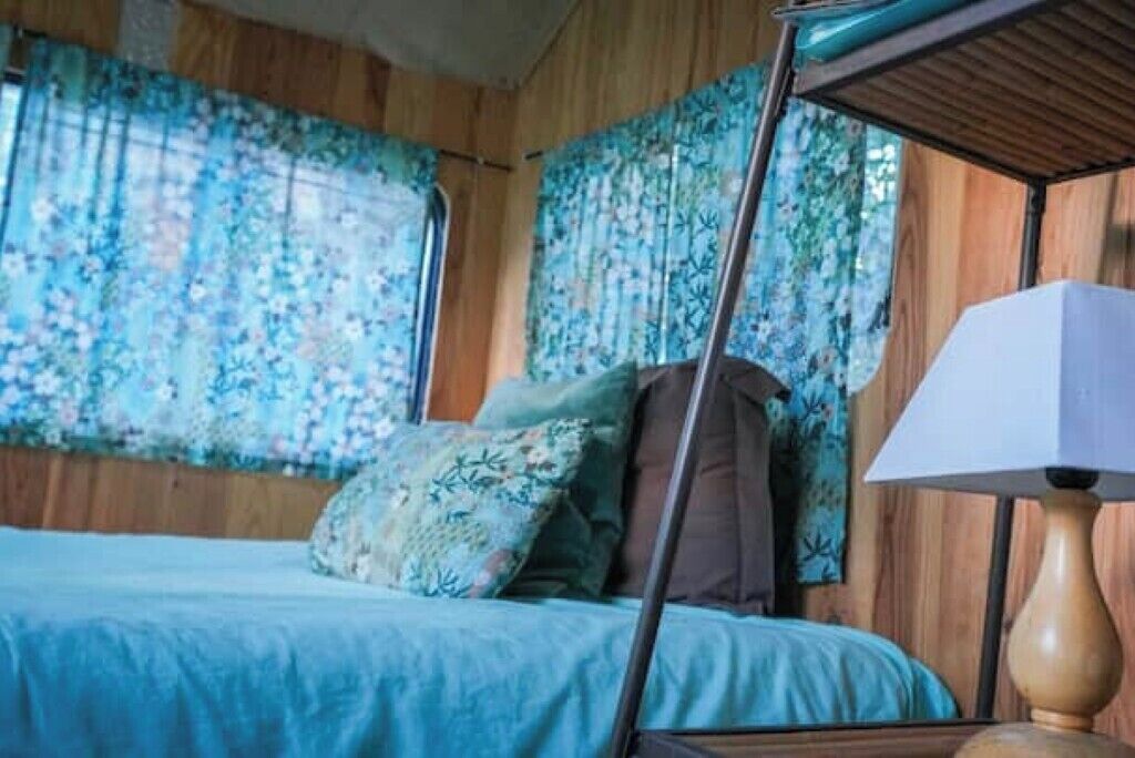 Een slaapkamer met een bed, een nachtkastje, een lamp en bloemen gordijnen.