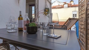 Een tafel gedekt met wijnglazen, flessen en een potplant op een balkon met uitzicht op gebouwen.