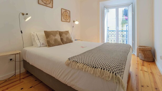 Een slaapkamer met een bed, bedlampen, een geweven mand en uitzicht op het exterieur.