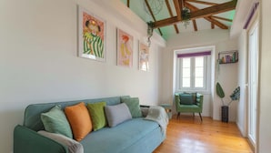 Een kamer met een groene bank, houten vloer, een raam en kunst aan de muur.