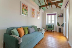 A room with a green sofa, wooden flooring, a window, and artwork on the walls. - 2BR ❤️ Terrace, AC, EV, Tram 28, Historic Center (Lisboa)