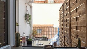 Uitzicht door een raam met een houten hek, een cactuso, een tafel met stoelen en een hangplant.