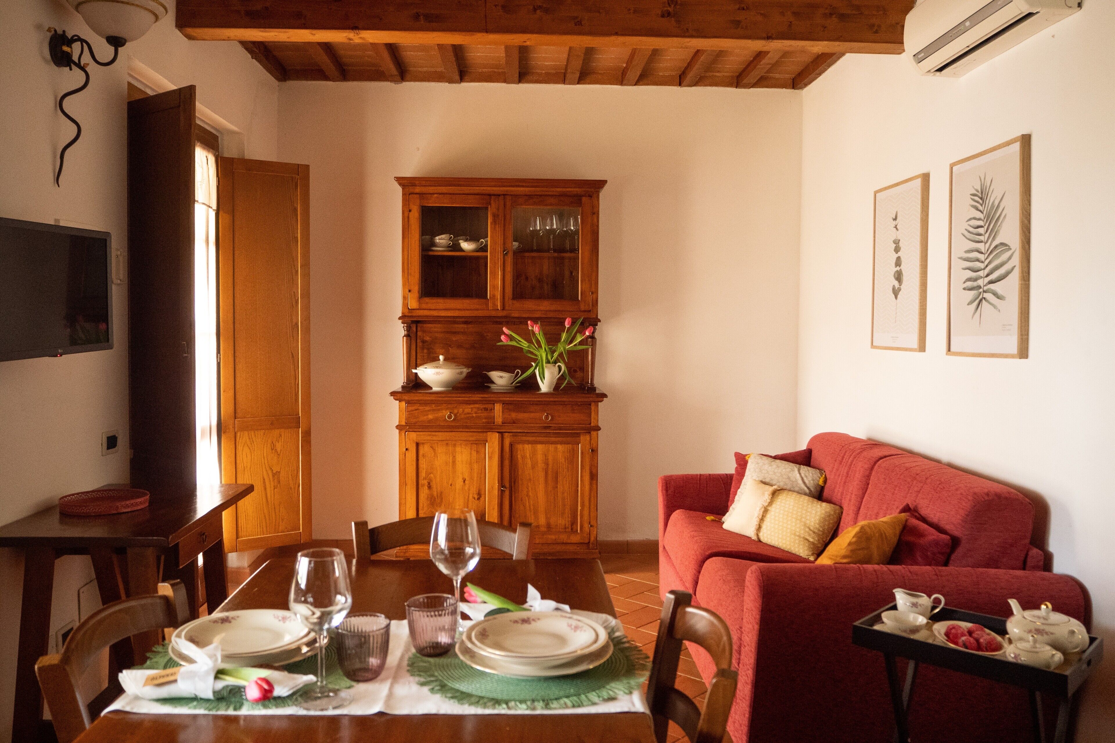Un comedor con una mesa de madera dispuesta para dos personas, un sofá rojo y un mueble con puertas de cristal.