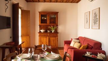Un comedor con una mesa de madera dispuesta para dos personas, un sofá rojo y un mueble con puertas de cristal.