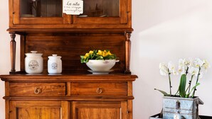 A wooden cabinet with a glass door, two white ceramic containers, a bowl with yellow flowers, and a small metal planter with white flowers.