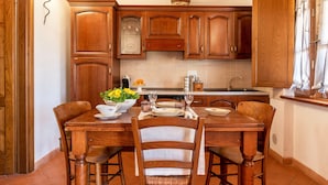 A wooden dining table with chairs, a kitchen area with wooden cabinets, and a window with curtains.