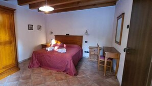 A bedroom with a large wooden wardrobe, a bed with a red bedspread, a bedside table with a lamp, and a small wooden desk. - Corte Belvedere (Sommacampagna)