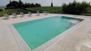 A rectangular swimming pool with clear water, surrounded by white lounge chairs and a sandy area.