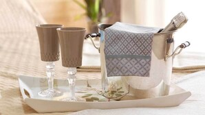 A tray with three glasses and a silver container with a patterned cloth cover, placed on a table with a floral design.