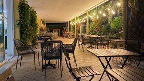An outdoor cafe area with tables and chairs, surrounded by greenery and plants.