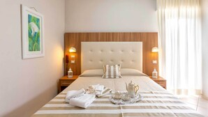 A neatly made bed with striped bedding, a bedside table with a lamp, a framed artwork, and a window with curtains.