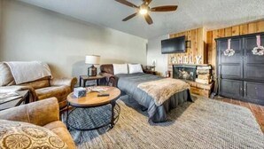 Ein gemütliches Zimmer mit einem Bett, zwei Sofas, einem runden Couchtisch, einem Deckenventilator, einem Fernseher und einem Kamin.