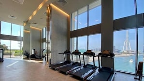 A gym with treadmills aligned against a wall with large windows overlooking a body of water and a bridge. - Vogue | 52 | 42 Marina near Ain Dubai | JBR Beach (Dubai)