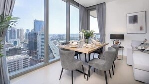 A modern dining area with a table set for four, large windows offering a city view, and a minimalist living space with a sofa and a TV. - Vogue | 52 | 42 Marina near Ain Dubai | JBR Beach (Dubai)