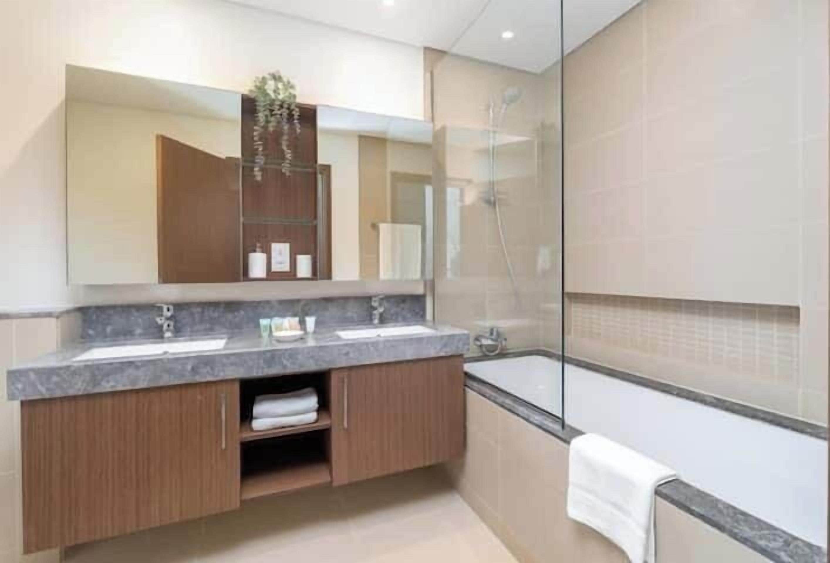 A modern bathroom with a double sink vanity, a glass shower enclosure, and a large mirror.