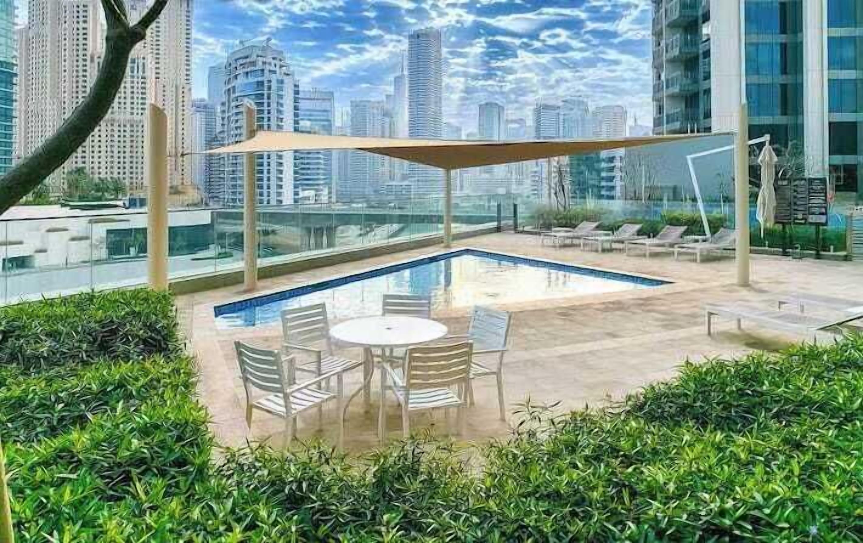 A rooftop pool area with a glass enclosure, lounge chairs, and a table.