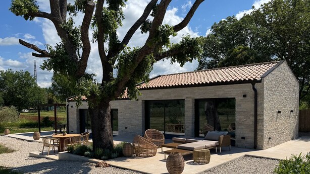 A modern outdoor patio area with a stone wall, wicker furniture, and a large tree providing shade. - 2-bedroom Poolvilla in Rovinj with cool AC breeze (Rovinj)
