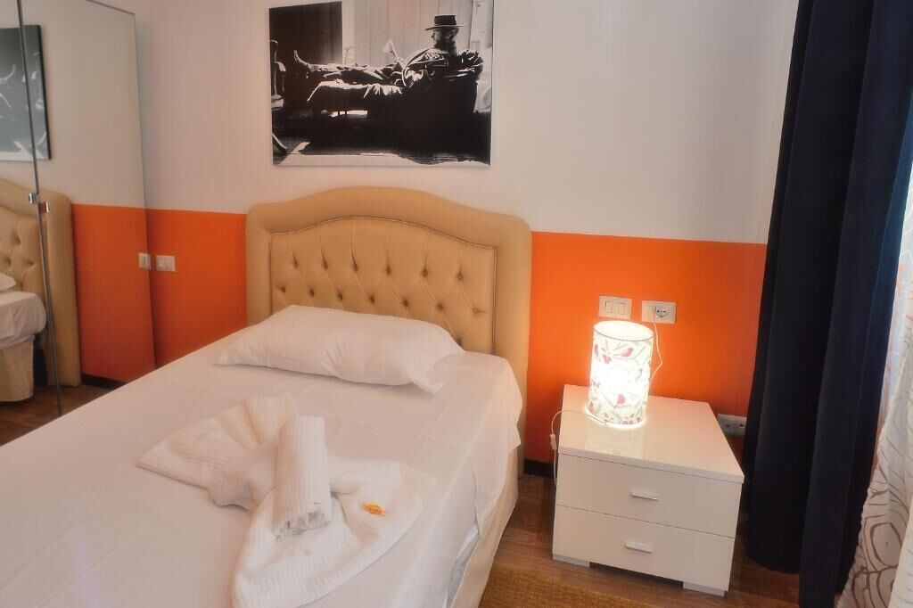 A hotel room with a bed, a nightstand, a lamp, and a framed picture on the wall.