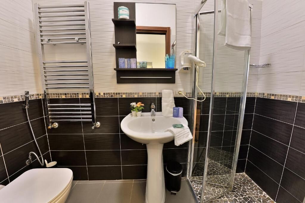 A bathroom with a white sink, a mirror, a towel rack, a shower, and a toilet.