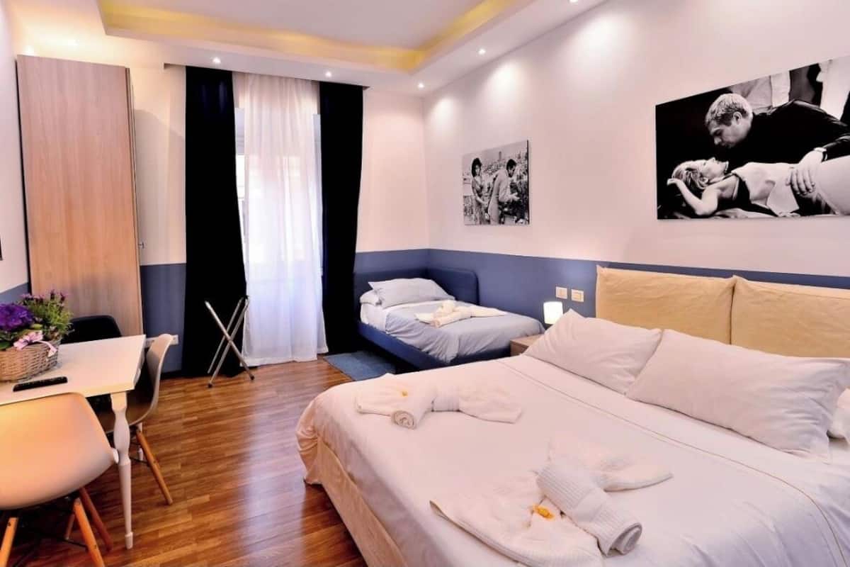 Habitación de hotel con una cama grande, una cama más pequeña, un escritorio con silla y una mesa de comedor.