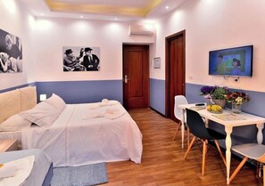 A hotel room with a bed, a desk with a chair, a TV, and wall art. - DolceVeneto (Rome)