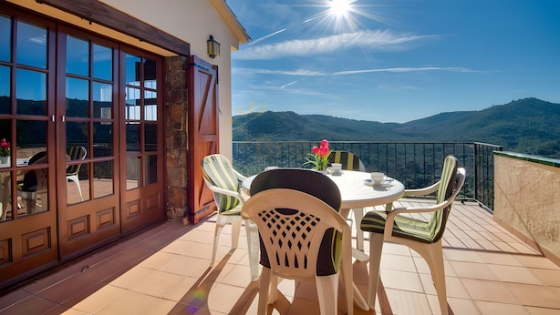 A balcony with a table and chairs, a view of the mountains, and a bright sun. - Beautiful House with Stunning Views (Calonge)