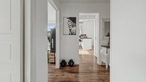 Un couloir doté d’un plancher en bois, de murs blancs et d’un coin cuisine situé au fond.