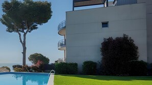 Ein Schwimmbecken mit Metallleiter, eine Rasenfläche, ein Baum und ein modernes Gebäude mit Balkonen.