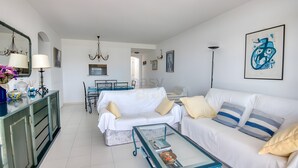 Ein modernes Wohnzimmer mit einem weißen Sofa, einem Glastisch und einem Essbereich mit Tisch und Stühlen.