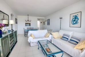 A modern living room with a white sofa, a glass coffee table, and a dining area with a table and chairs. - Wonderfull Sea View  (Calonge)