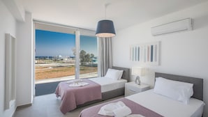 A hotel room with two beds, a large window with a view of the city, a ceiling fan, and an air conditioning unit. - 5 & 6 OP Villas Fig Tree Bay Protaras Bedrooms 8, Bathrooms 6, Sleeps 20 (Protaras)