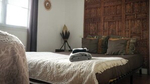 A bedroom with a large bed, a decorative headboard, a wall-mounted sun decoration, and a small table with a lamp. - Nomad Room (Corcoué-sur-Logne)