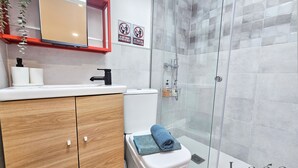 Ein modernes Badezimmer mit Toilette, Waschbecken und Dusche. Zwei Schilder an der Wand weisen darauf hin, keine Toilettenpapier in der Toilette und keine Papierhandtücher zu entsorgen.